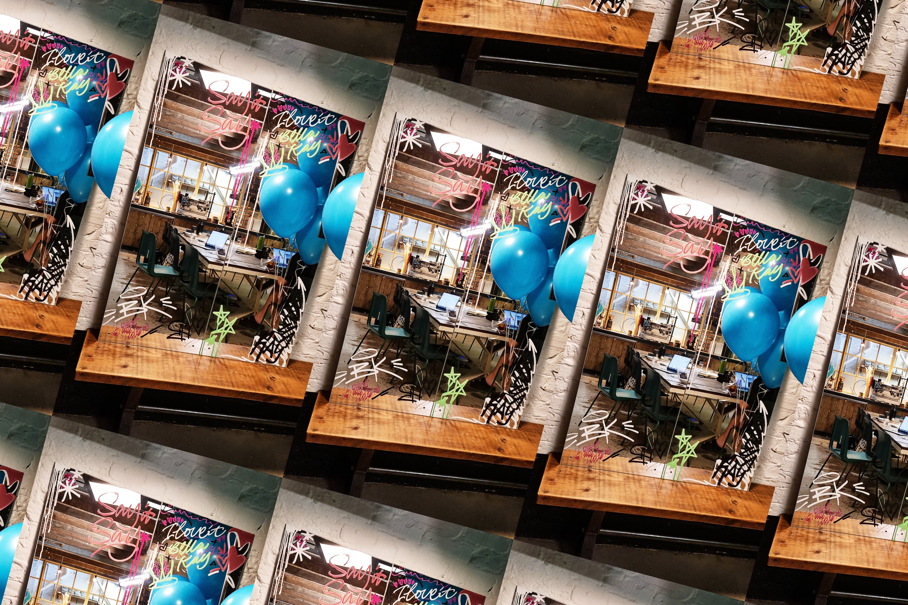Live spray-lettering artwork reading 'Say it Say, I love it Bella Kay' on a mirror with blue balloons at the Bella Kay event